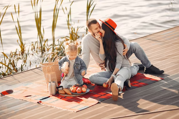 Family picnicking by the water on a wooden pathway
